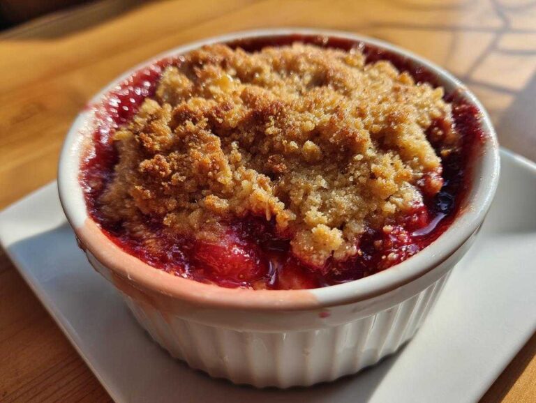 Close-up of a freshly baked Strawberry Rhubarb Crisp bubbling in a white ramekin with a golden brown topping.