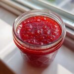 Top-down view of a canning jar filled with vibrant, textured Strawberry Rhubarb Soda Syrup glowing in sunlight.
