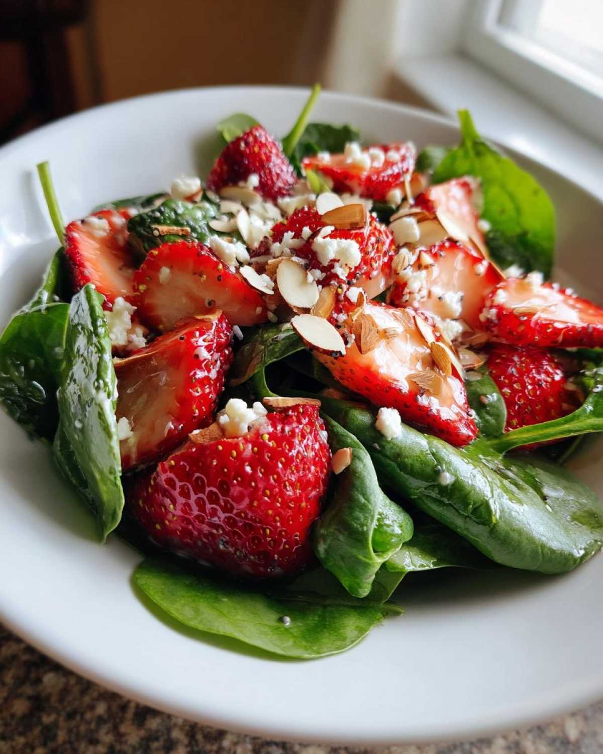 A close-up of a vibrant Strawberry Spinach Salad topped with feta cheese and sliced almonds, ready to be dressed.