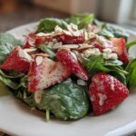 A vibrant close-up of Strawberry Spinach Salad with Poppyseed Dressing, featuring fresh strawberries, spinach, almonds, and feta.