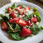 Close-up of a vibrant Strawberry Spinach Salad with poppyseed dressing, sliced strawberries, almonds, and feta cheese.