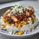 A close-up of a Street Corn Chicken Bowl Recipe featuring sliced, seasoned chicken over rice and charred corn, topped with cotija cheese.