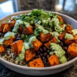A close-up of a vibrant Sweet Potato & Black Bean Quinoa Bowls topped with creamy green sauce and fresh cilantro.
