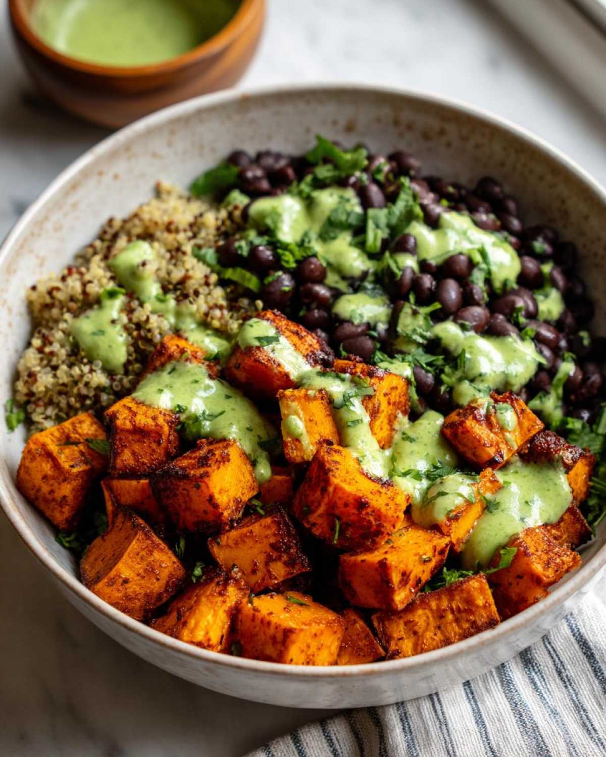 Close-up of a Sweet Potato & Black Bean Quinoa Bowls featuring roasted sweet potatoes, black beans, quinoa, and a creamy green dressing.