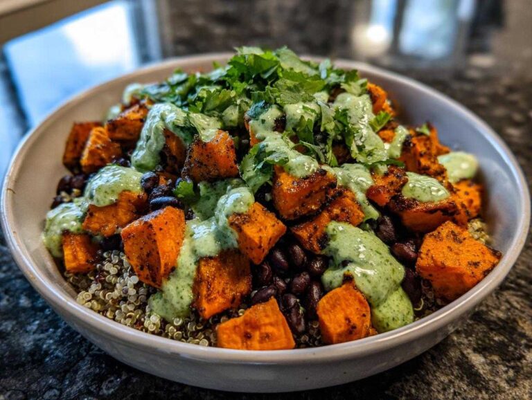A close-up of a vibrant Sweet Potato & Black Bean Quinoa Bowls topped with creamy green sauce and fresh cilantro.