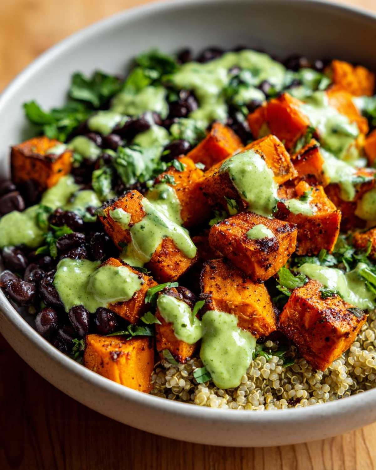 Close-up of a bowl filled with Sweet Potato & Black Bean Quinoa Bowls, topped with roasted sweet potatoes and green dressing.