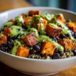 A close-up of a bowl filled with Sweet Potato & Black Bean Quinoa Bowls, topped with a creamy green sauce.