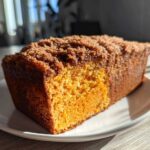 A close-up of a slice of moist Sweet Potato Cinnamon Bread with a rich, dark brown crumb topping resting on a white plate.