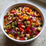 Close-up of a white bowl filled with colorful Texas Caviar, featuring black-eyed peas and diced peppers and onions.