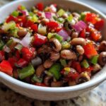 Close-up of a white bowl filled with colorful Texas Caviar, featuring black-eyed peas, red peppers, and onions.