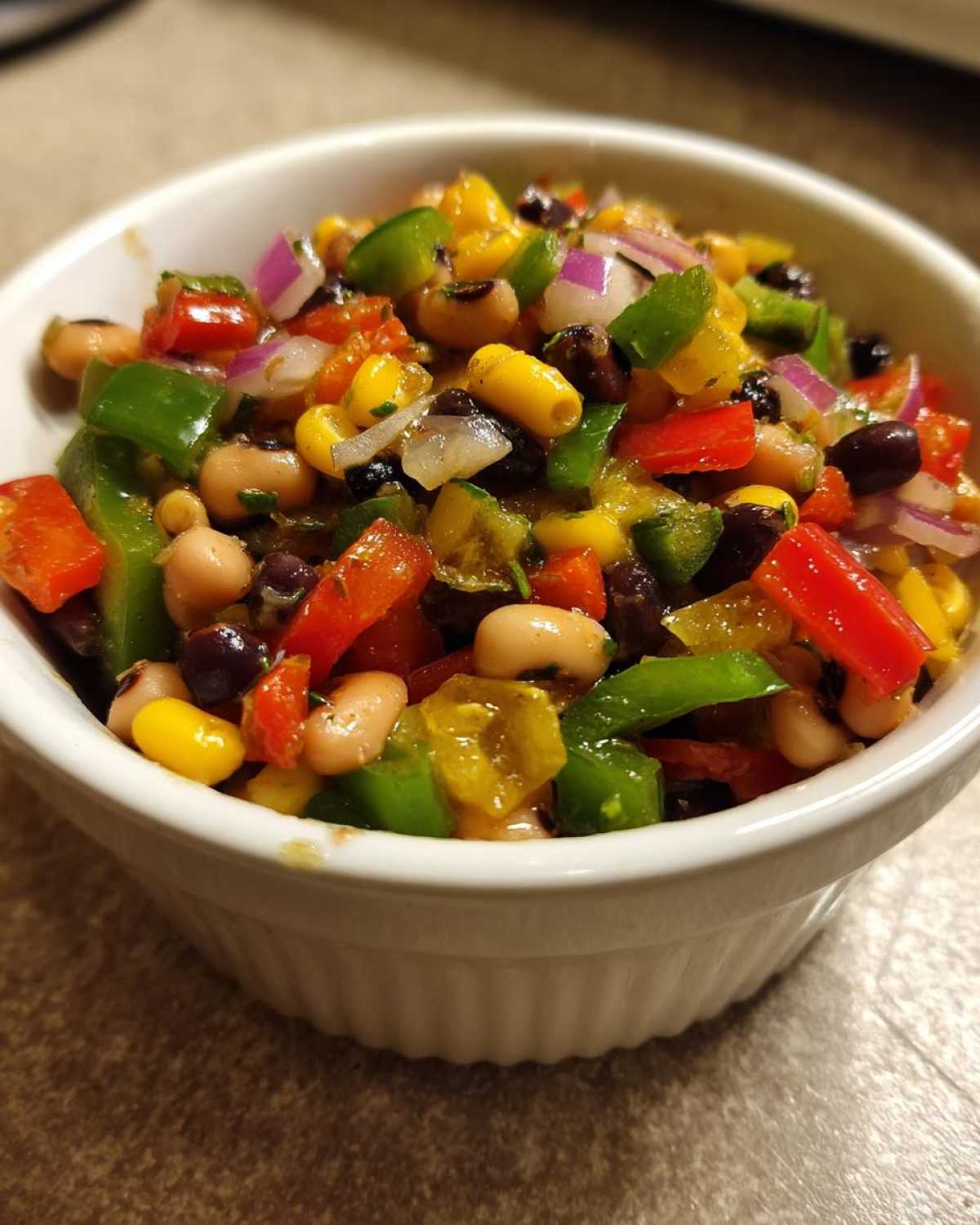 Close-up of vibrant Texas Caviar in a white bowl, featuring black beans, corn, peppers, and onions.