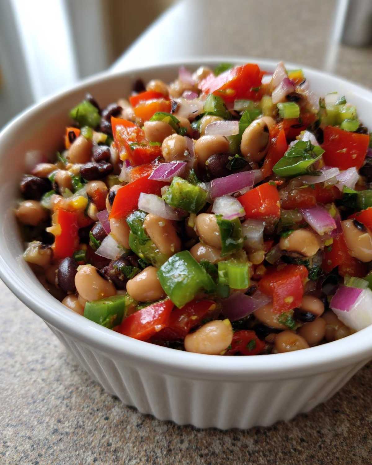 A close-up of vibrant Texas Caviar featuring black-eyed peas, red onion, bell peppers, and cilantro in a white bowl.