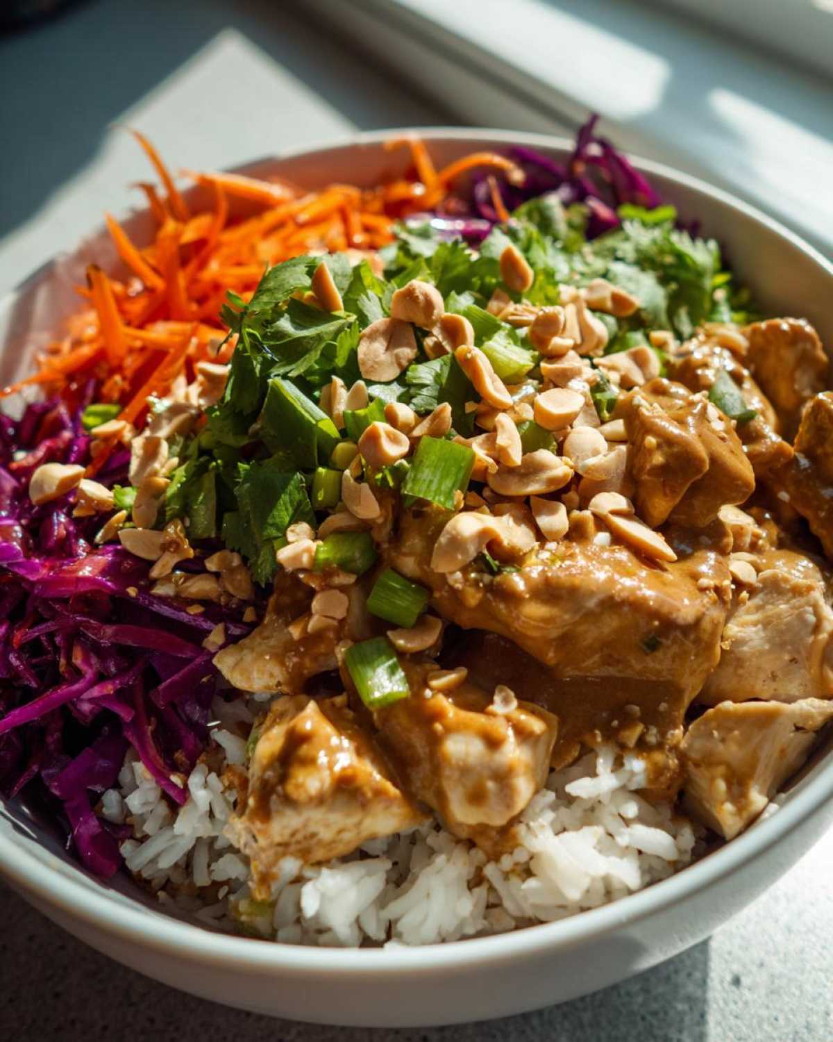 A vibrant bowl featuring Thai Peanut Chicken Crunch Bowls over white rice, topped with shredded carrots, red cabbage, cilantro, and chopped peanuts.