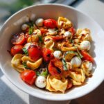 Close-up of a bowl filled with Tortellini Caprese Salad featuring tortellini, cherry tomatoes, mozzarella balls, and balsamic glaze.
