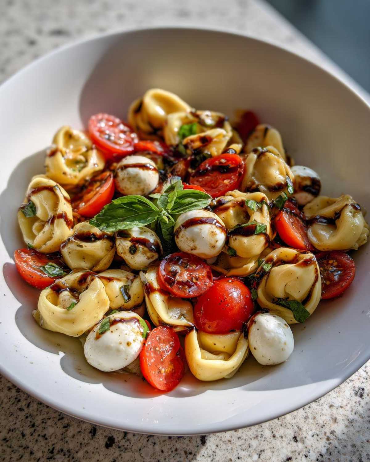 Close-up of a Tortellini Caprese Salad Recipe featuring tortellini, cherry tomatoes, mozzarella balls, and balsamic glaze.