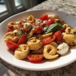A bright white bowl filled with Tortellini Caprese Salad Recipe featuring tortellini, halved cherry tomatoes, mozzarella balls, and basil.