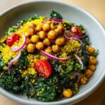 Close-up of a vibrant bowl featuring turmeric roasted chickpeas, kale, yellow quinoa, and red onion slices.