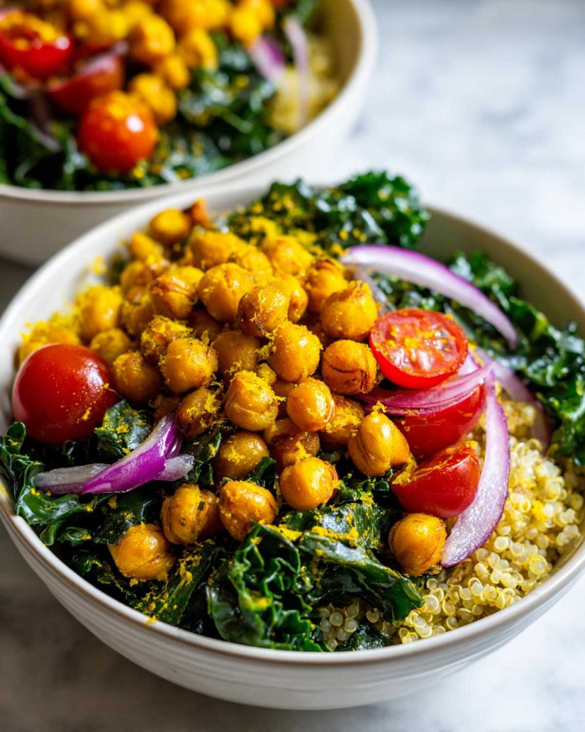 Close-up of a vibrant Turmeric Roasted Chickpea & Kale Bowls featuring golden chickpeas, dark green kale, red onion, and cherry tomatoes over quinoa.
