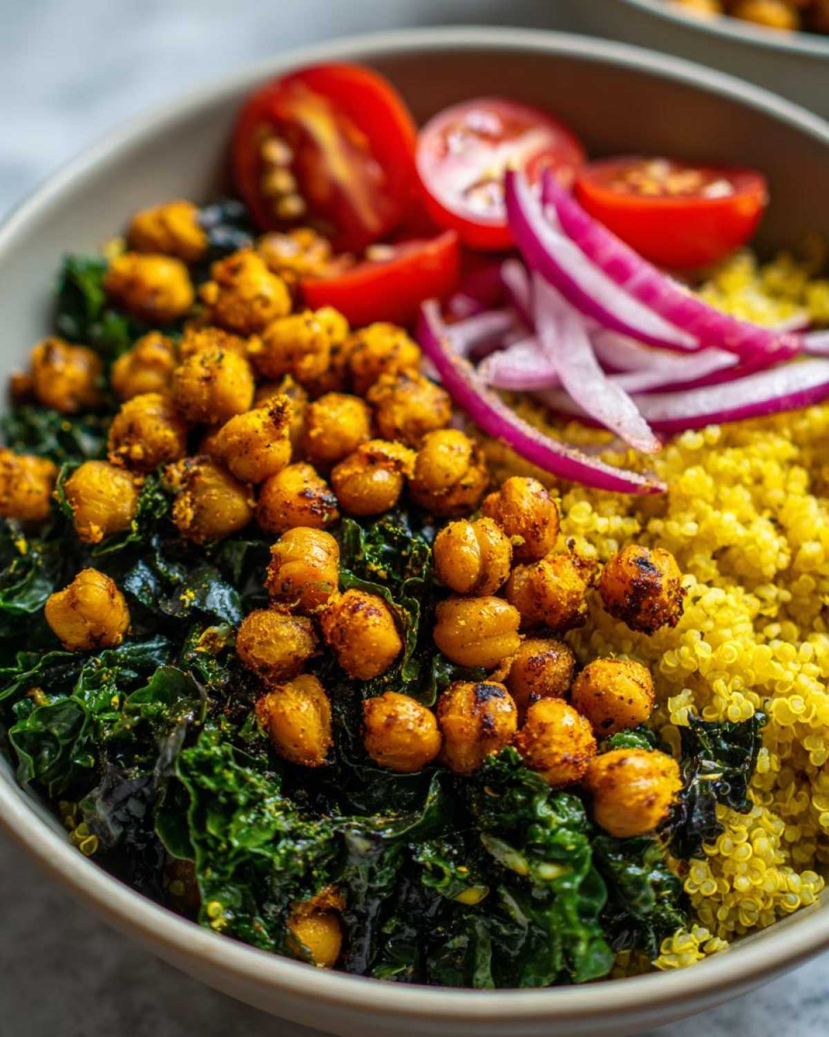 Close-up of a healthy bowl featuring turmeric roasted chickpeas, sautéed kale, yellow quinoa, and fresh toppings.