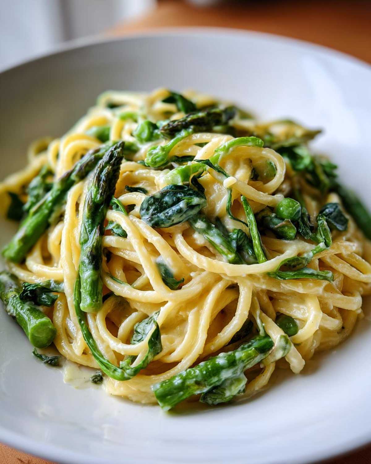 Close-up of creamy Vegan Lemon Asparagus Pasta tossed with bright green asparagus spears and greens in a white bowl.