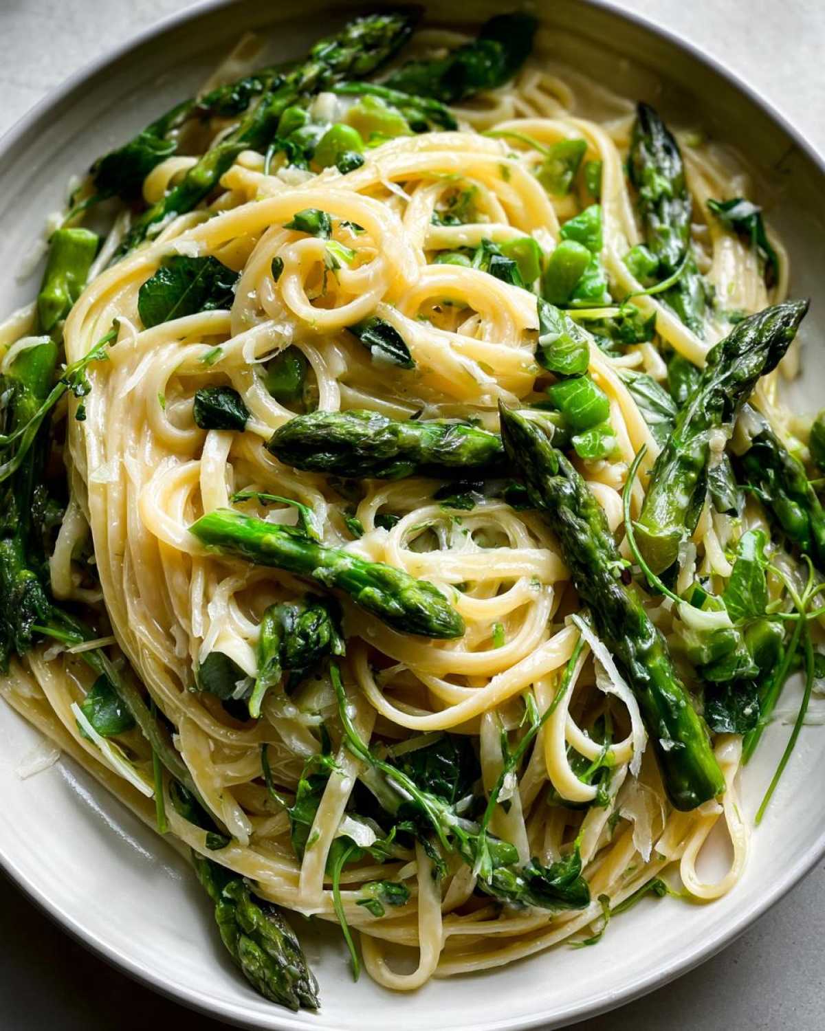 A close-up overhead view of creamy Vegan Lemon Asparagus Pasta tossed with bright green asparagus spears and pea shoots.