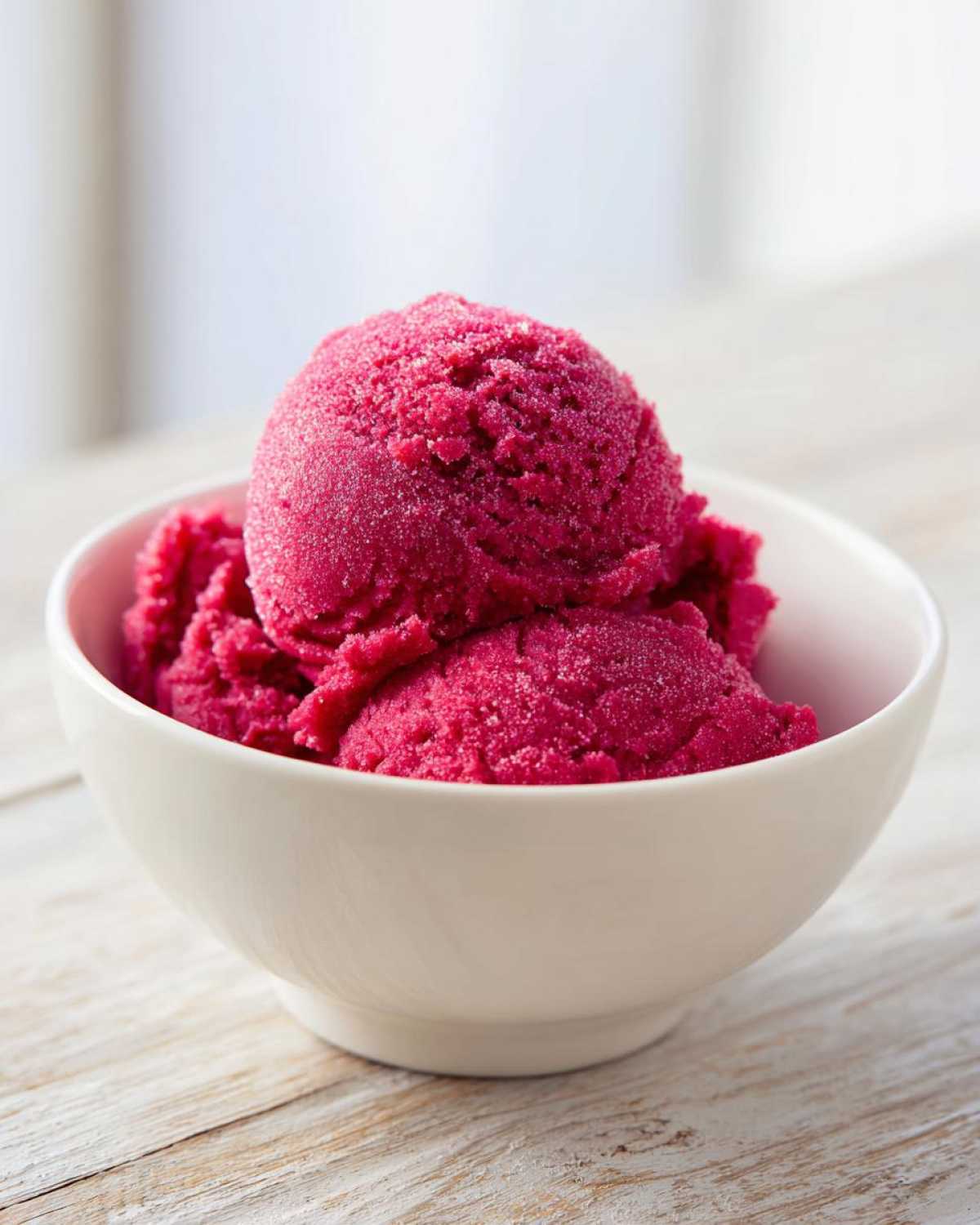 Two scoops of bright pink Raspberry Sorbet dusted with fine ice crystals in a white bowl.