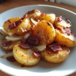 Close-up of warm potatoes, onions, and bacon pieces, resembling a warm dressing for german potato salad.