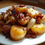 Close-up of warm German potato salad featuring golden potatoes, caramelized onions, and crispy bacon bits on a white plate.