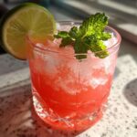 Close-up of a vibrant Watermelon Lime Refresher filled with crushed ice, garnished with a lime wheel and fresh mint.
