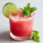 Close-up of a vibrant Watermelon Lime Refresher filled with crushed ice, garnished with a lime wheel and fresh mint sprigs.
