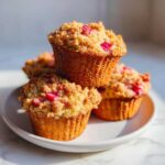 A stack of three golden Whole Wheat Rhubarb Streusel Muffins topped with crumbly streusel and visible pink rhubarb pieces.