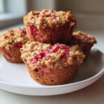 A stack of four freshly baked Whole Wheat Rhubarb Streusel Muffins topped with crunchy streusel and visible pink rhubarb pieces.