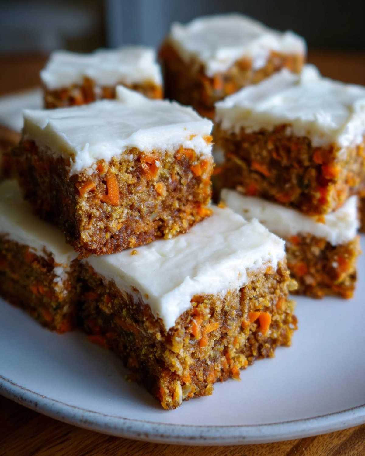 Stack of moist Zucchini Carrot Bars recipe squares topped with thick white cream cheese frosting on a light plate.