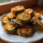 A pile of golden brown, breaded Air Fryer Zucchini slices stacked on a white, scalloped plate.