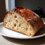 Close-up of a perfectly baked artisan sourdough bread loaf cut in half, showing an open, airy crumb structure. These are great Sourdough Recipes Need Try.