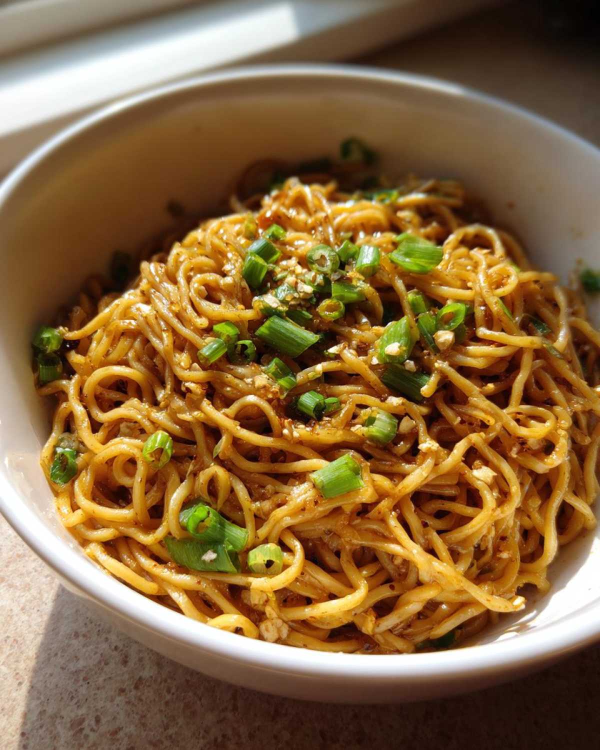 A close-up view of glossy Asian Garlic Noodles tossed in sauce and topped with fresh chopped green onions.