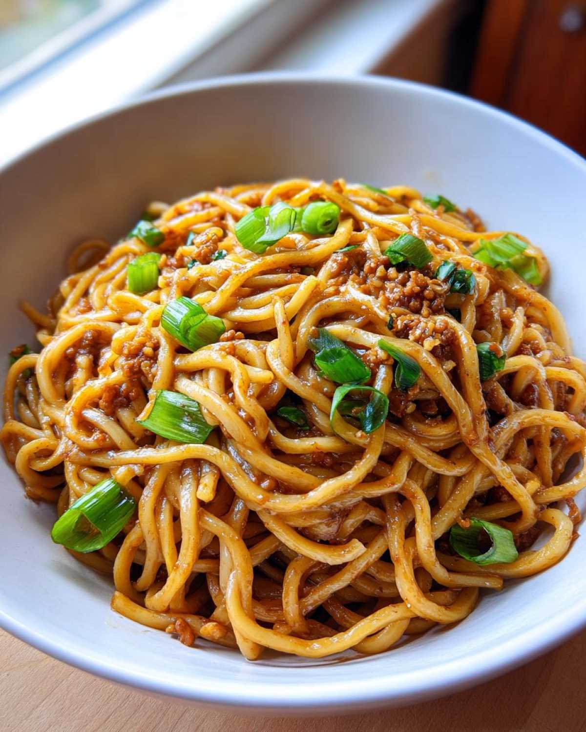 A close-up shot of glossy Asian Garlic Noodles coated in a savory sauce and topped with fresh green onions.
