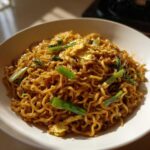 A close-up of glossy Asian Garlic Noodles tossed with scrambled egg pieces and bright green scallions in a white bowl.