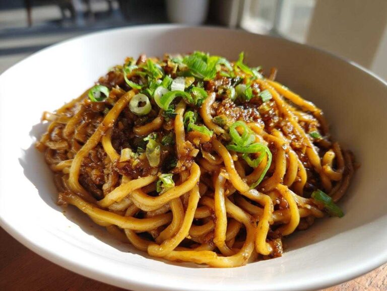 A close-up shot of glossy, thick Asian Garlic Noodles coated in a dark sauce and topped with fresh green onions.