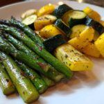 Close-up of roasted asparagus spears next to chopped zucchini and yellow squash seasoned with herbs.