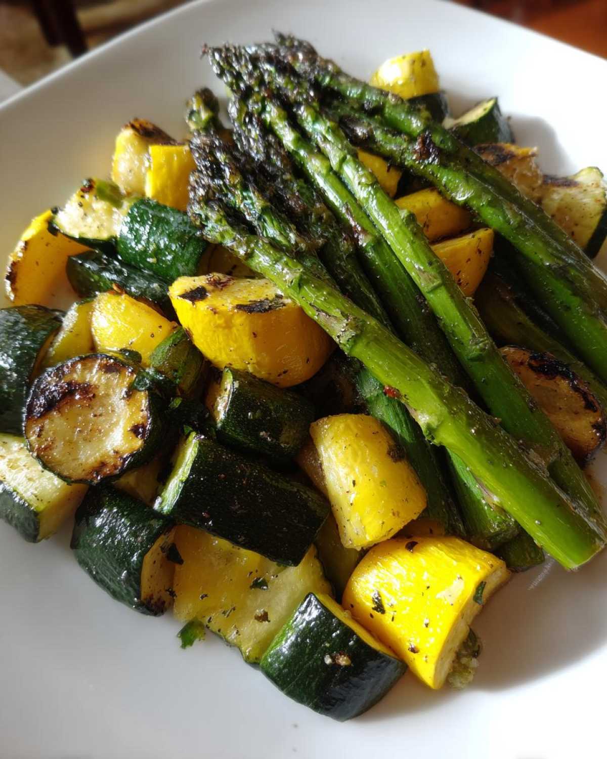 Close-up of roasted asparagus with chunks of yellow squash and zucchini, seasoned and served on a white plate.