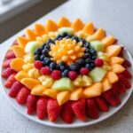A stunning Baby Bloom Fruit Platter arranged in a flower shape with strawberries, cantaloupe, blueberries, and raspberries.