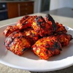 A pile of vibrant red, charred pieces of Baked Tandoori Chicken Oven on a white plate.