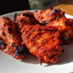 Close-up of four pieces of vibrant red Baked Tandoori Chicken Oven, showing slight charring on a white plate.