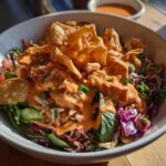 Close-up of a vibrant Bang Bang Salmon Salad topped with creamy orange sauce and crispy wonton strips.