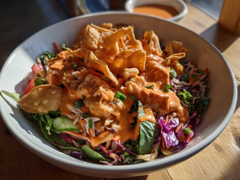 Close-up of a vibrant Bang Bang Salmon Salad topped with creamy orange sauce and crispy wonton strips.