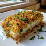 A close-up of a flaky fillet of Boston Baked Cod topped with golden brown breadcrumbs and fresh parsley.