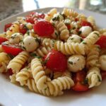 A close-up of a serving of Caprese Pasta Salad featuring rotini pasta, cherry tomatoes, and small mozzarella balls.