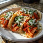 Four delicious Chicken Al Pastor tacos served on a white plate, topped with diced white onion and cilantro.