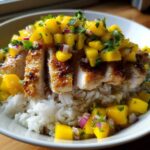 A close-up of a Chicken Mango Rice Bowl featuring sliced, seared chicken breast over white rice, topped with bright mango salsa.